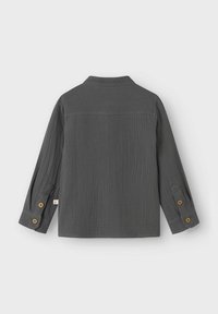 Camicia grigia con bottoni, realizzata in un tessuto texture, presenta un colletto, maniche lunghe con possibilità di risvolto e bottoni marroni sui polsini.