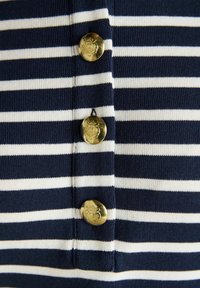Tissu à rayures bleu marine et blanc avec trois boutons dorés verticaux gravés d'un blason, centrés le long des rayures.