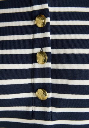 Marineblaue und weiße Streifenstoff mit drei vertikalen goldenen Knöpfen, die mit einem Wappen graviert sind und mittig entlang der Streifen angeordnet sind.