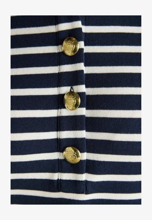 Marineblaue und weiße Streifenstoff mit drei vertikalen goldenen Knöpfen, die mit einem Wappen graviert sind und mittig entlang der Streifen angeordnet sind.