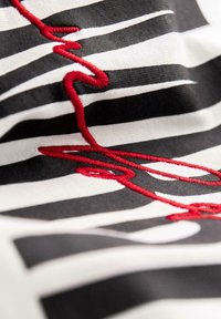 Tela de rayas en negro y blanco con una línea bordada roja prominente, creando un contraste visual texturizado. El diseño presenta curvas dinámicas.