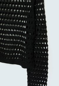 Tissu en maille noire avec motif de trous ouverts en rangées horizontales, montrant une manche et une partie d’un vêtement sur un fond clair.