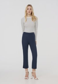 Pantaloni navy a scampanatura con una silhouette aderente, realizzati in un tessuto liscio. Abbinati a una maglietta a maniche lunghe bianca a righe e sandali bianchi con tacco.