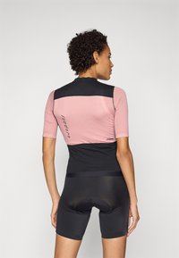 Rosa sykkeltrøye med korte ermer har en strukturert svart panel på baksiden og svarte sykkelshorts med polstret sete.