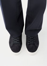 Black suede sneakers with gray laces and white rubber soles, viewed from above, paired with navy pants.