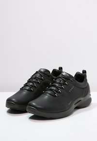 Scarpe sportive nere con tomaia in pelle perforata, lacci elastici e suola ammortizzata. Presentano dettagli con logo e un design snello.