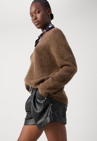 Brun strikket sweater med løs pasform og tekstureret overflade, parret med sorte lædershorts med opsmøget kant og detaljer i sølvhardware.