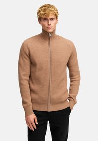 Beige ribbad stickad zip-up tröja med hög krage och l ånga ärmar, med en slät dragkedja och detaljer i texturerad tyg.