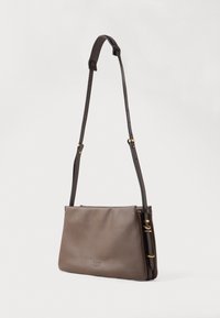 Hnědá kožená crossbody taška s nastavitelným popruhem na rameno a decentně embosovaným logem na přední straně na čistém bílém pozadí.