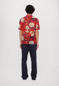 Lyhythihainen punainen paita, jossa on suuri kukkakuosi valkoisena, keltaisena ja sinisenä. Yhdistetty tummansiniisiin housuihin, näkyy takaa.