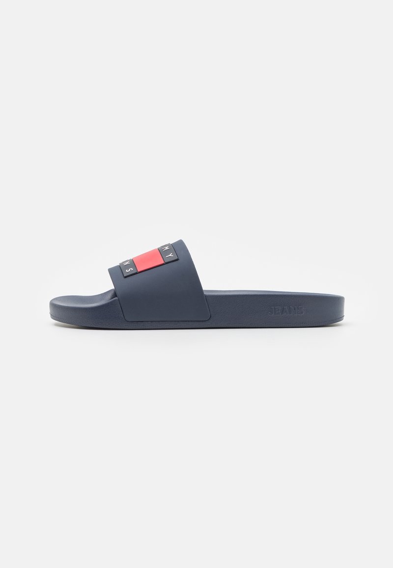 Sandale claquette bleu marine avec une large bride ornée de blocs de logo rouges et blancs et un marquage en relief sur le côté de la semelle.