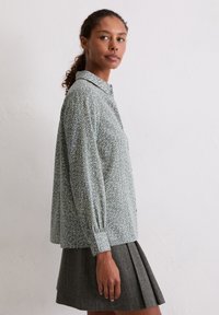 Jasnoniebieska koszula w kwiaty na guziki z długimi rękawami i marszczonymi mankietami, zestawiona z ciemnoszarą plisowaną spódnicą. Tkanina o fakturze.