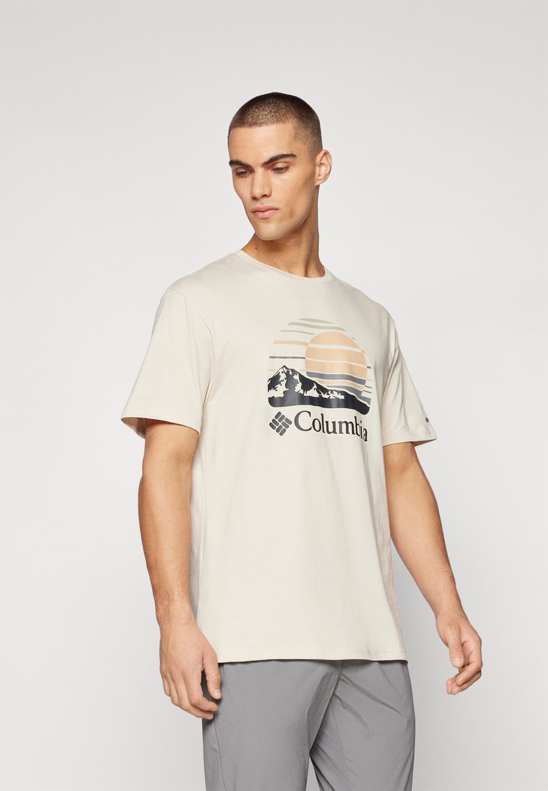 Beige katoenen T-shirt met een afbeelding van bergen en een zonsondergang, met groene en perzikkleurige strepen, en het Columbia-logo in zwart.