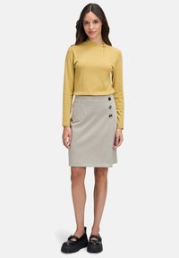 Musztardowa bluzka z długim rękawem z marszczeniem, w połączeniu z kraciastą spódnicą z trzema czarnymi guzikami i boczną kieszenią. Grube czarne buty.