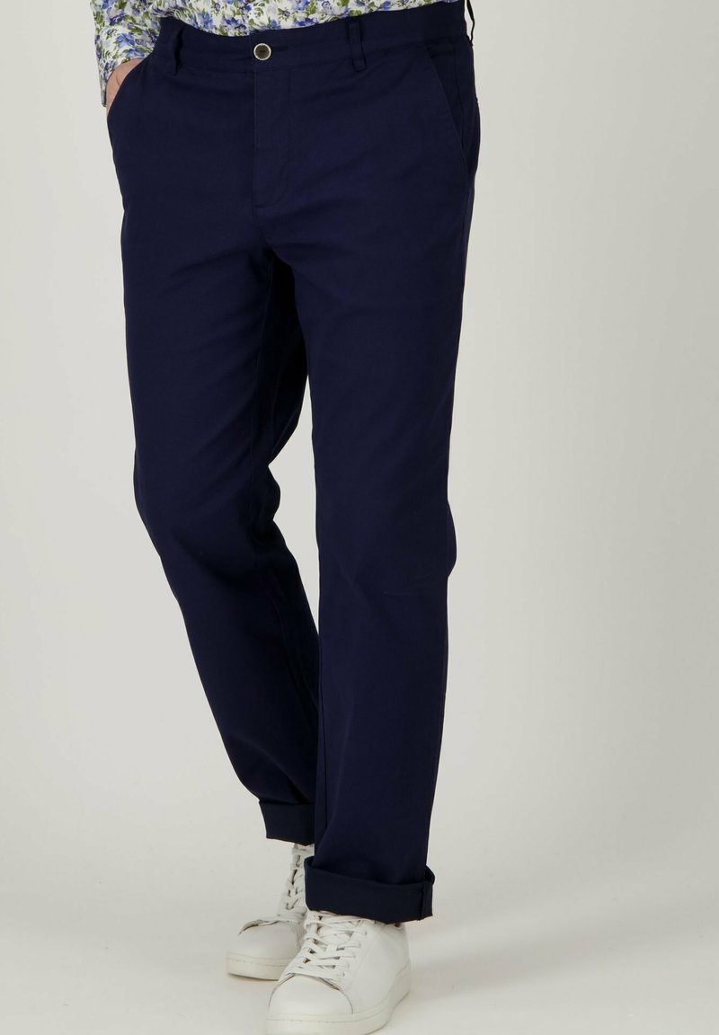 Donkerblauwe katoenen broek met zichtbare voorzakken, een platte voorkant en opgerolde mouwen, gecombineerd met witte sneakers.