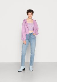 Um hoodie cropped lavanda sobre um top cropped canelado lilás, combinado com jeans de perna reta azul claro e botins azul claro com um salto preto.