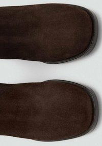 Brązowe zamszowe botki za kostkę z kwadratowym noskiem i gładką czarną gumową podeszwą. Materiał jest miękki, bez widocznych elementów metalowych ani wzorów.