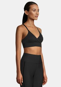 Sujeción deportiva negra con un diseño de escote en V, tirantes finos y una textura suave y elástica. Combinada con leggins negros de talle alto.