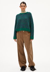 Groene luipaardprint gebreide trui met paarse accenten, gecombineerd met bruine corduroy wijde broekspijpen en zwarte gestructureerde schoenen.