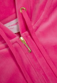 Fuksijos spalvos džemperis su minkšta tekstūra, su auksiniu užtrauktuku, raišteliais ir etikete viduje. Lygus audinys su jaukiu išvaizda.