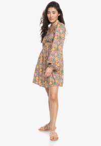Vestido floral con un patrón multicolor, mangas abullonadas y cintura elástica; combinado con sandalias ligeras. Tejido texturizado, hasta la rodilla.