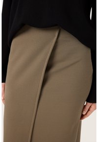 Khaki sukně vyrobená z hladké tkaniny s skrytým předním švem, spojená s černým topem, který zobrazuje jednoduchý, čistý design.