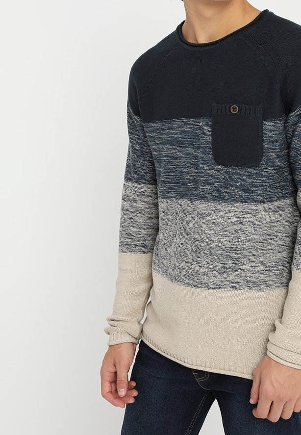 Homme portant un pull en maille à manches longues en color block avec des sections bleu marine, gris et beige et une poche poitrine à boutons.