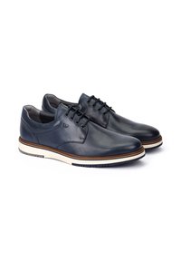 Scarpe in pelle blu navy con una texture liscia, punta arrotondata, suola bianca e accento marrone attorno al sottopiede. Design con sei occhielli per i lacci.