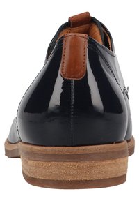 Chaussure habillée en cuir noir brillant avec un tirant en cuir marron et une semelle en bois empilée, vue de l'arrière.