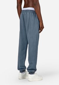 Pelēki treniņbikses ar elastīgu jostasvietu un potīšu gumijām, kas izceļas ar maigu tekstūru. Apvienotas ar baltām sporta kurpēm, veidojot ikdienišķu izskatu.