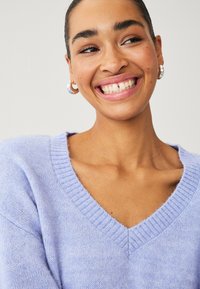 Pull à col en V lavande en maille douce, avec des accents côtelés au niveau de l'encolure et de l'ourlet, et une coupe décontractée. Texture lisse.