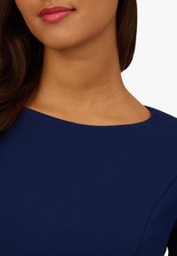 Marineblaues Kleid mit glatter Textur, runder Ausschnitt und figurbetontem Oberteil, das klare Linien und ein minimales Design betont.