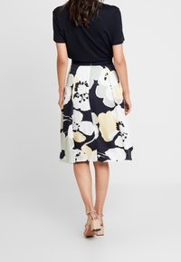 Kukkahame, jossa on mustaa, valkoista ja pastellivärejä, virtaavaa kangasta, puolipitkä malli, yhdistetty mustaan toppiin ja beigeihin kenkiin.