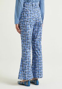 Pantaloni svasati con fantasia blu e design geometrico; il tessuto sembra liscio. Abbinati a scarpe basse con motivo blu.