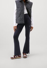 Grå quiltad ärmlös väst, vit långärmad topp, marinblå utsvängda byxor och vinröda och vita sneakers med en Nike-logga på varje plagg.