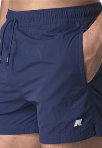 Pantaloni da bagno navy con vita elasticizzata, cordoncino, tasche laterali e una piccola etichetta con logo. Il tessuto sembra leggero e con una texture.