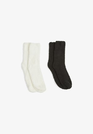 Due paia di calzini pelosi: uno bianco e uno nero. Entrambi hanno una consistenza morbida e un design standard di lunghezza crew.