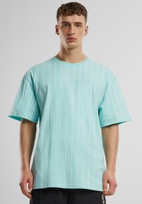 T-shirt turquoise à manches courtes avec des rayures verticales blanches, encolure ronde et logo brodé sur la poitrine. Matière en coton.