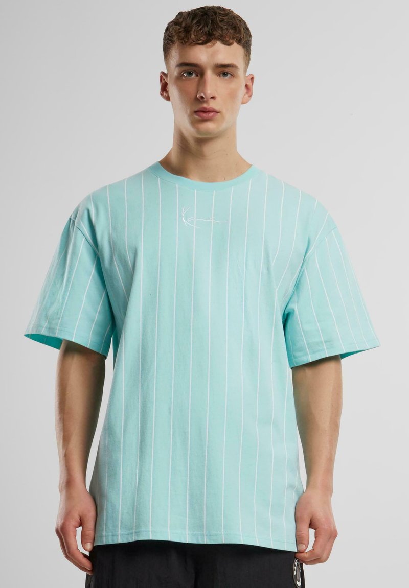 T-shirt turquoise à manches courtes avec des rayures verticales blanches, encolure ronde et logo brodé sur la poitrine. Matière en coton.