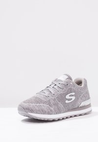 Grå träningsskor tillverkade av stickat material, med en strukturerad ovandel, rund tå, snörning och en vit gummisula med logodetalj.