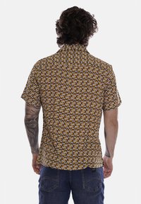 Camicetta a maniche corte con un motivo circolare giallo e marrone. Realizzata in tessuto leggero, presenta un colletto standard e una vestibilità comoda.
