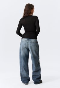 Top nero a maniche lunghe abbinato a jeans di jeans azzurri oversized. I jeans presentano due tasche posteriori e una vestibilità comoda.