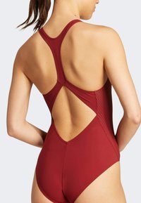 Reddish-burgundy one-piece swimsuit with a racerback design, open back cutout, and subtle ribbed texture on lower sides.