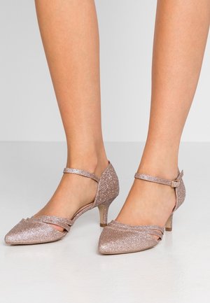 Tacones de purpurina en oro rosado con punta afilada, tira en el tobillo y tacón bajo tipo kitten. Presenta un detalle entrecruzado en el empeine para un diseño adicional.