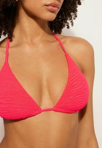 Rosa triangelformad bikinitopp med texturerad tyg, tunna justerbara axelband och en jämn yta. Har ett vågigt mönster och minimalt med beslag.