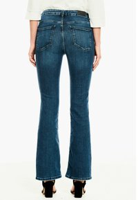 Jeans de mezclilla acampanados en azul oscuro con una textura suave. Presenta dos bolsillos traseros y un dobladillo sin terminar. Combinados con sandalias de tacón negro.