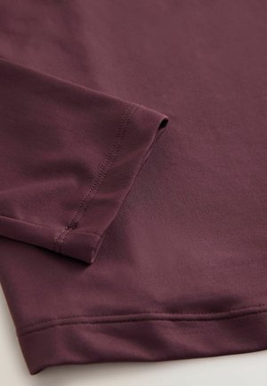 Bordeaux-kangas lähikuvassa, jossa on sileä rakenne, käänteet hihassa, hienovarainen venyvyys ja tarkka ompelu reunoilla.