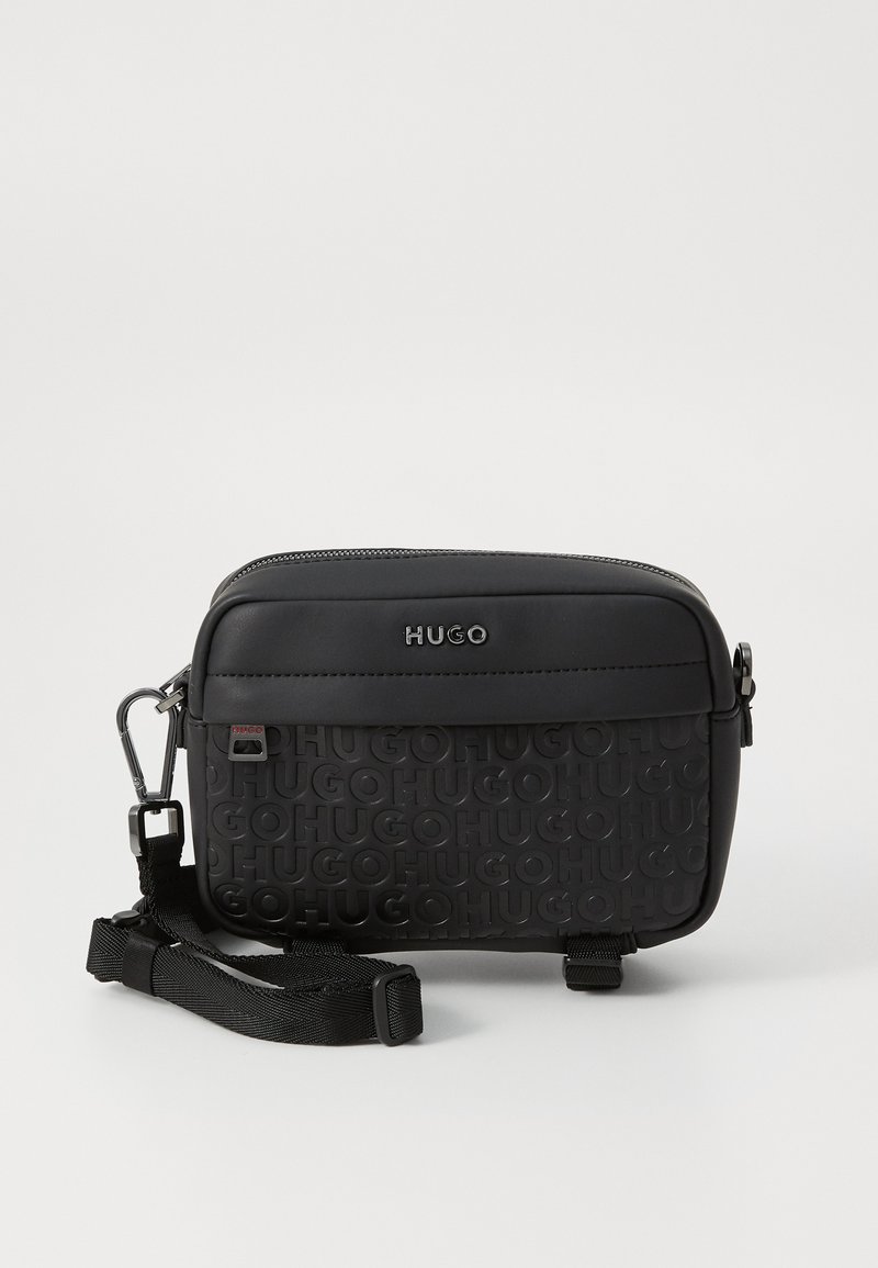 Black crossbody bag with textured Hugo logo, smooth top section, zipper closure, adjustable strap, and metallic hardware accents.