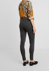 Grå smala byxor med en slät textur, med bakfickor med blixtlås. Matchas med en blus med flerfärgat mönster.