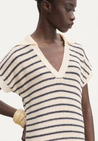 Striped knit top in cream with navy stripes, featuring a V-neck and short sleeves. Smooth texture with a relaxed fit. Minimalist design.